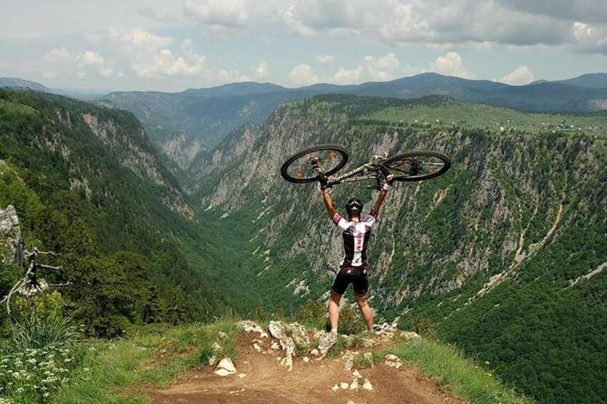 a man holding up his bike on top of a mountain