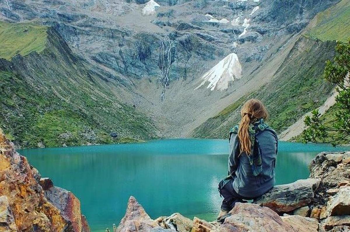 una donna seduta su una roccia che domina un lago di montagna