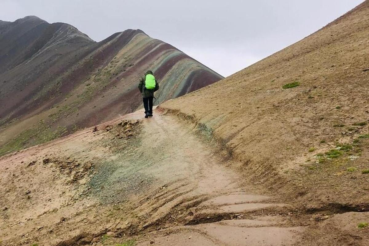 una persona con una giacca verde che cammina su una collina sterrata