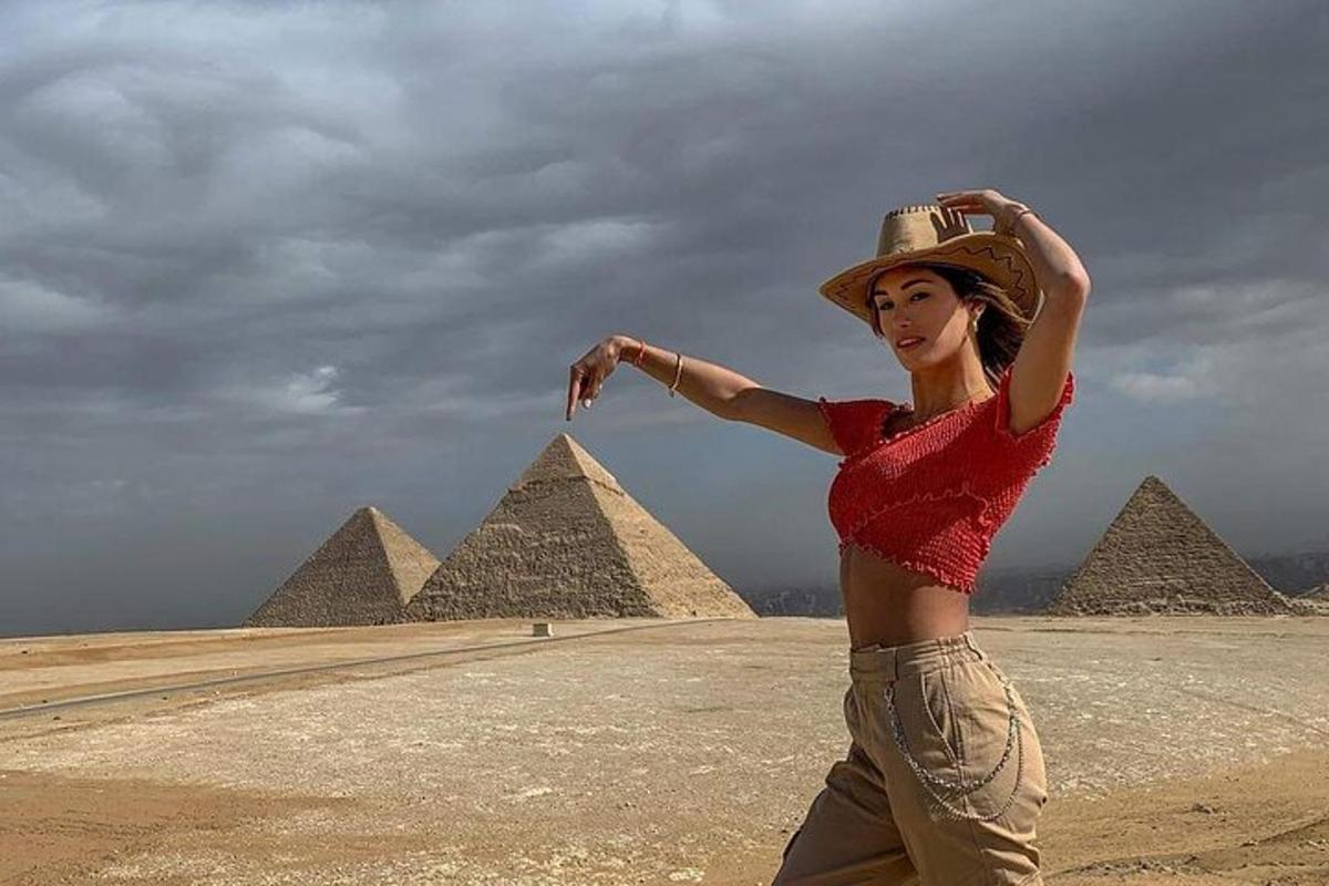 Una mujer con sombrero parada frente a las pirámides.