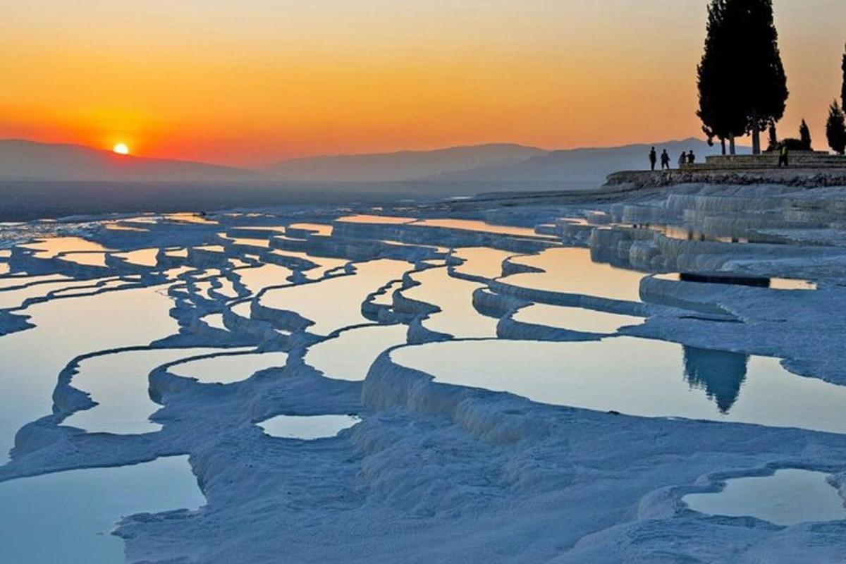 persone in piedi su una collina che guardano il tramonto sulla neve