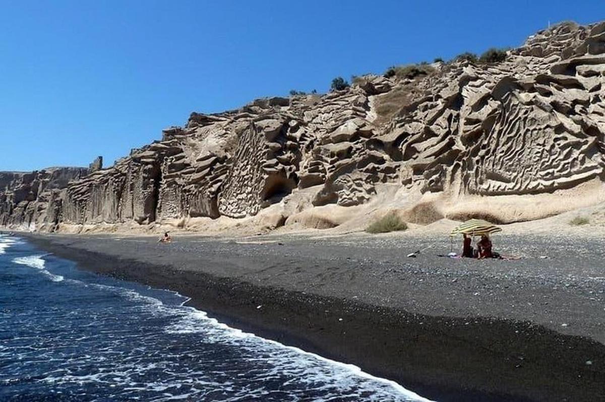 μια μαύρη παραλία με ανθρώπους να στέκονται κάτω από μια ομπρέλα