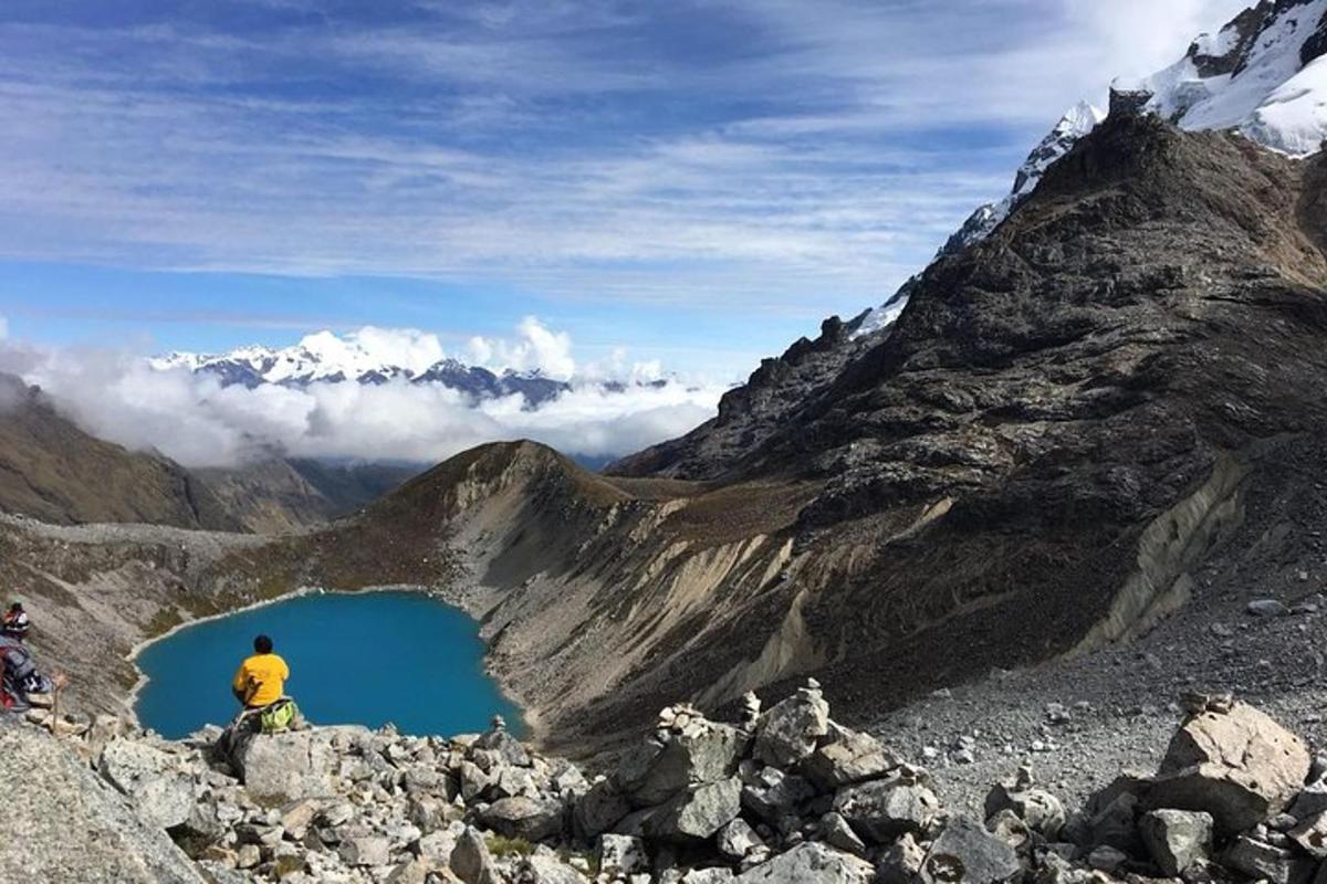 seorang pria duduk di puncak gunung yang menghadap ke danau biru