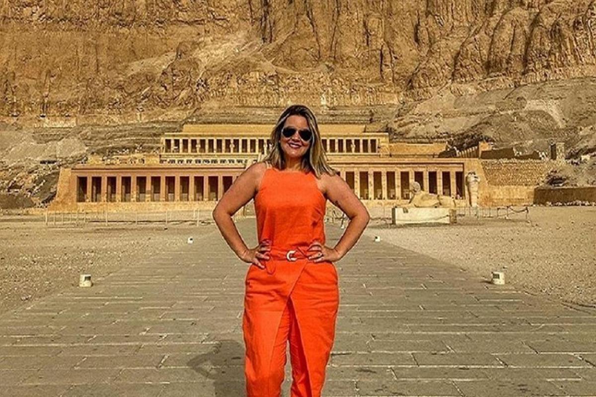 Μια γυναίκα με πορτοκαλί φόρεμα στέκεται μπροστά σε ένα κτίριο