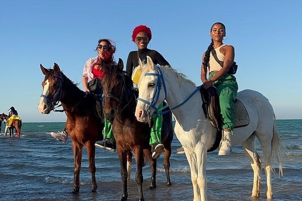 tiga orang sedang menunggang kuda di pantai