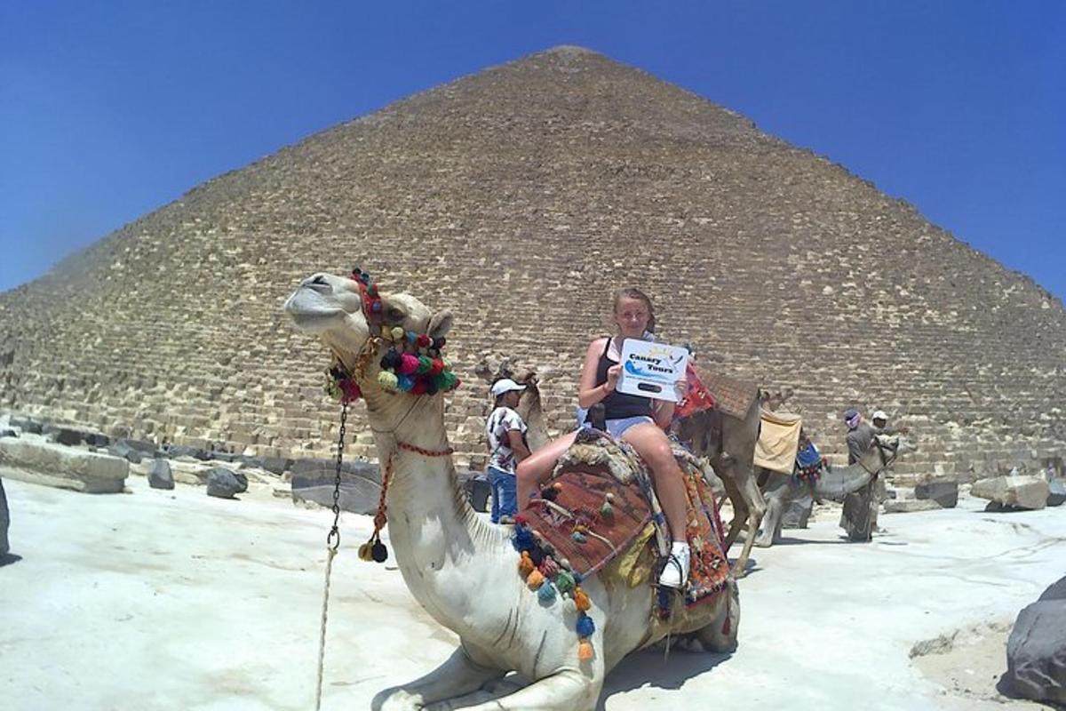 o femeie călare pe o cămilă în fața unei piramide