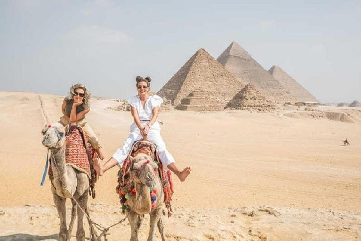 two people riding on camels in front of the pyramids
