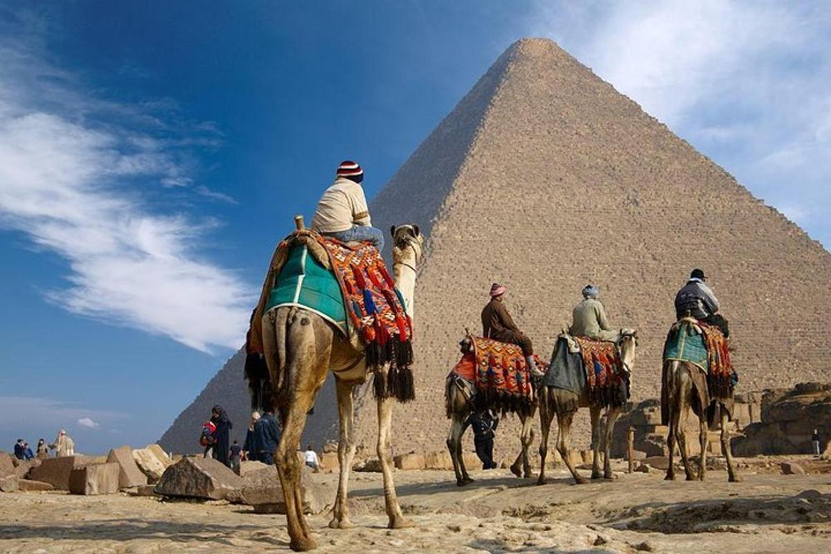 ryhmä ihmisiä ratsastaa kameleilla pyramidien edessä