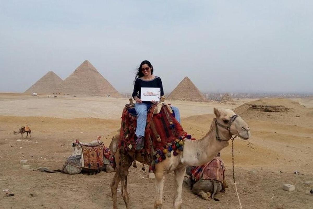 a woman sitting on a camel in front of the pyramids