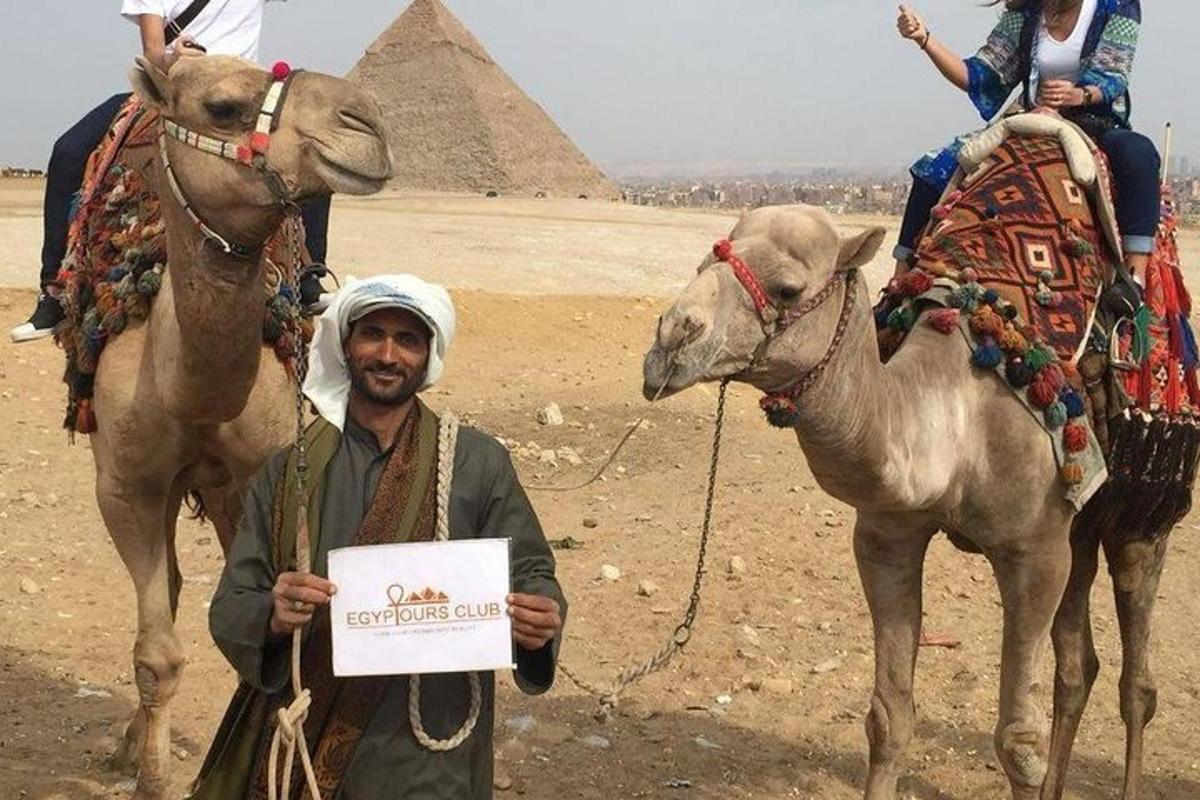muž držící ceduli vedle velblouda a pyramid