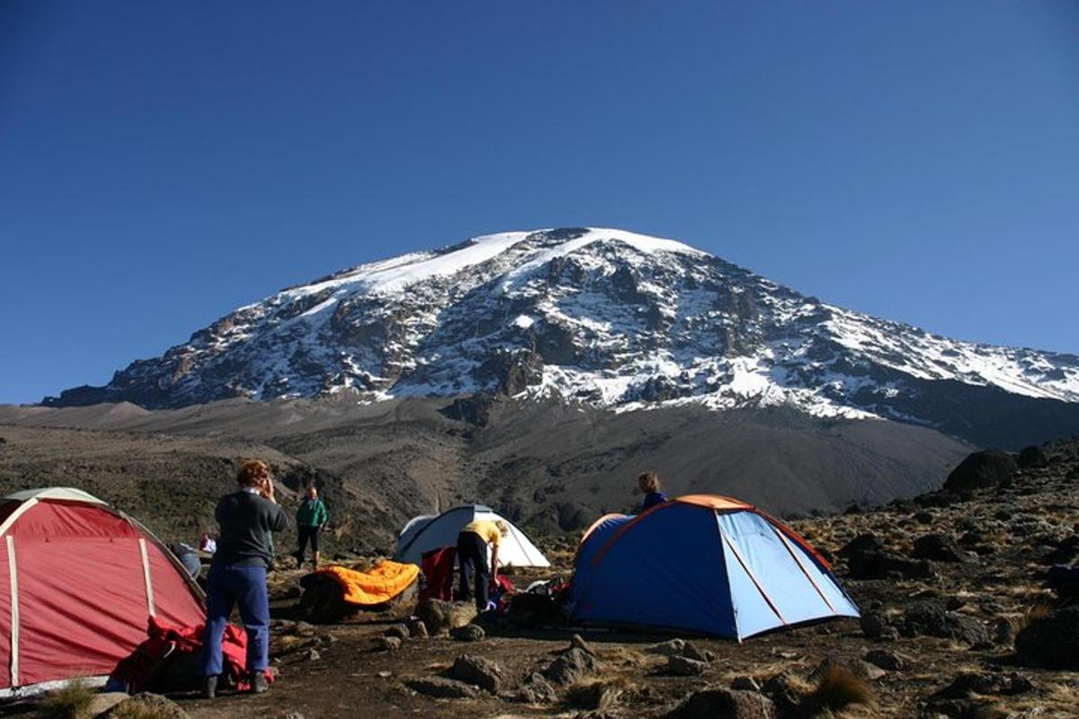 um grupo de pessoas em pé ao redor de tendas em frente a uma montanha