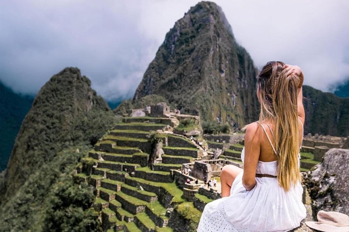 uma mulher de vestido branco sentada em um penhasco olhando para ruínas