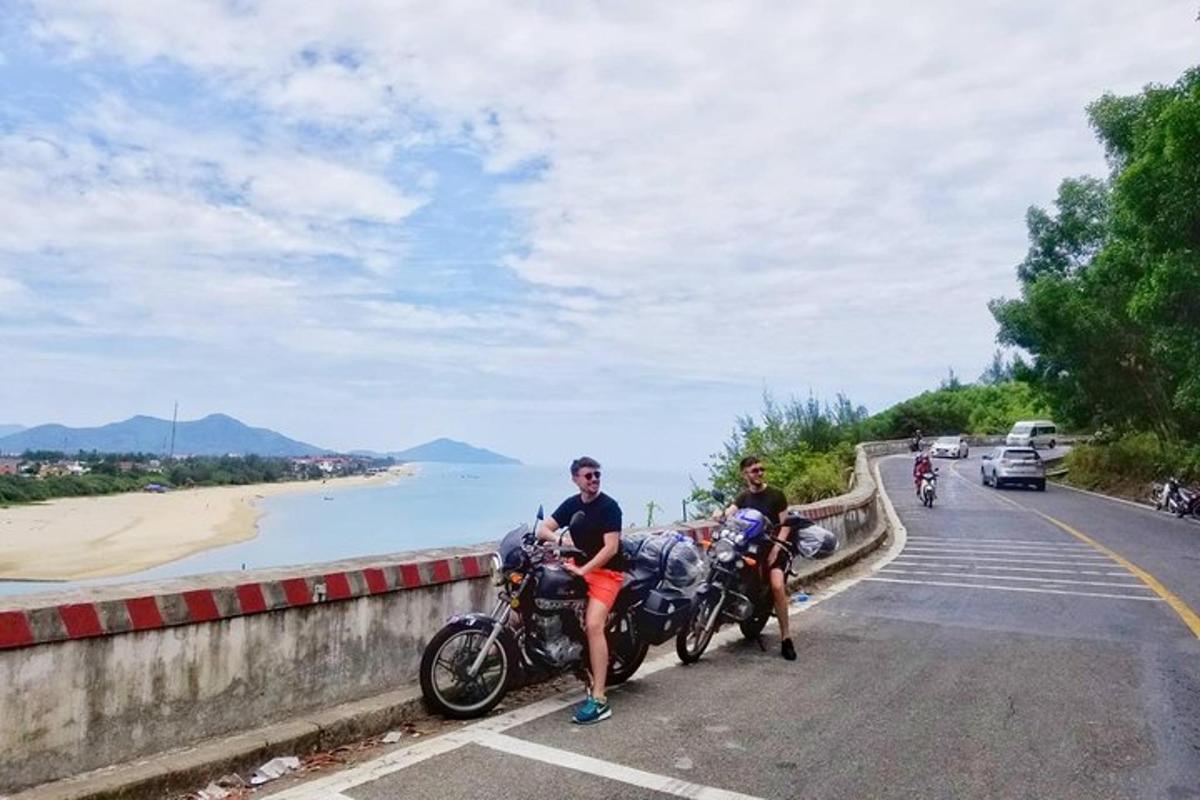 Dos personas viajando en motocicleta por una carretera cerca del océano.