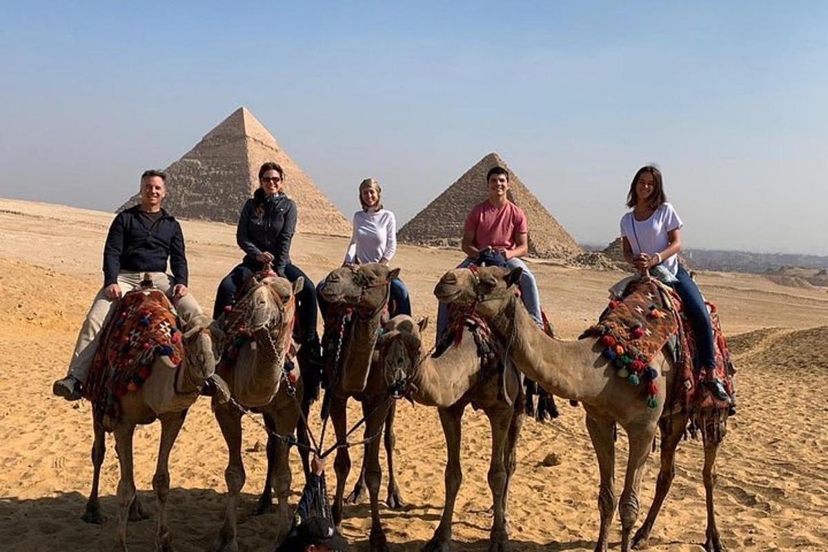 Un grupo de personas montando camellos frente a las pirámides.