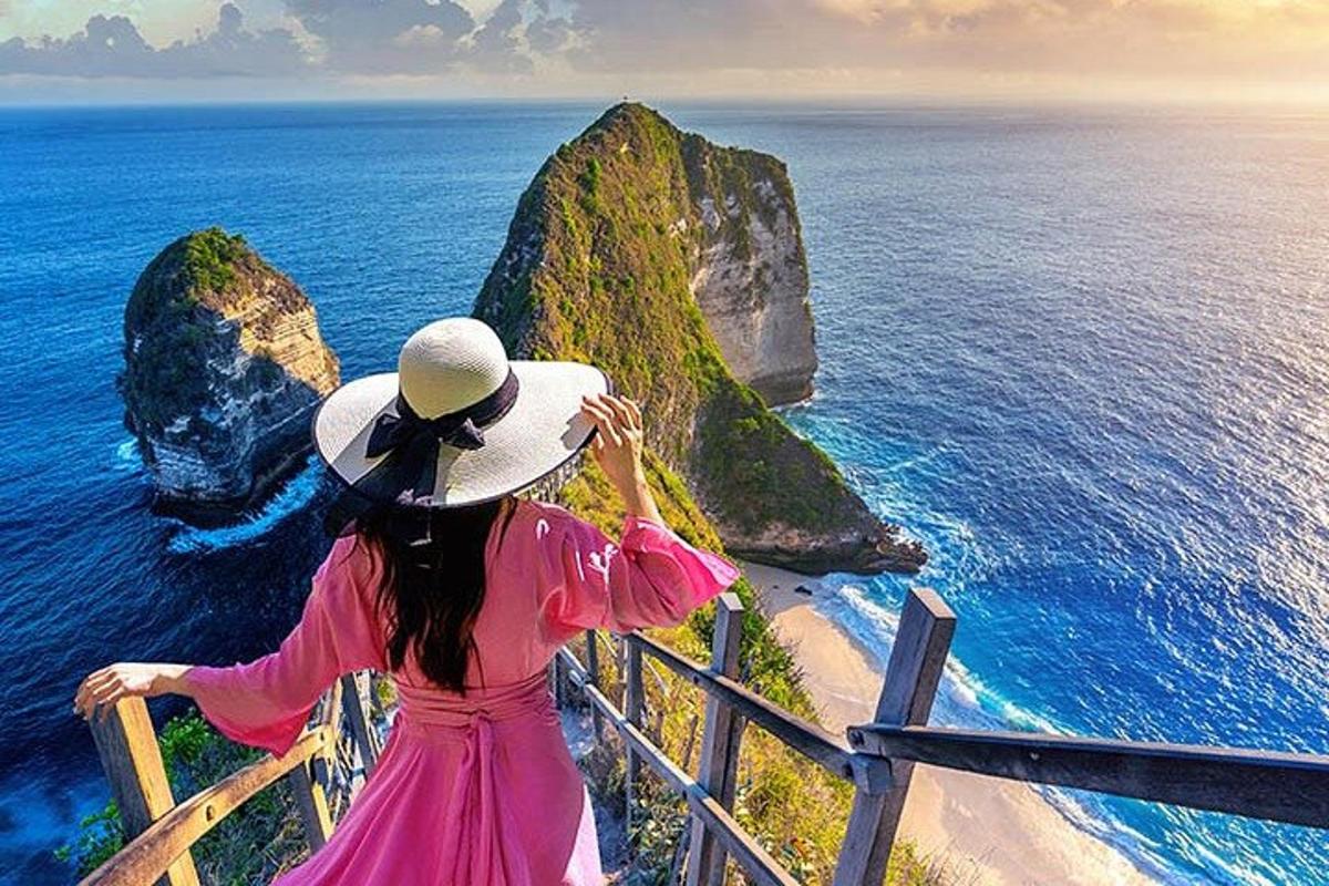 una dona amb un vestit rosa i un barret mirant l'oceà