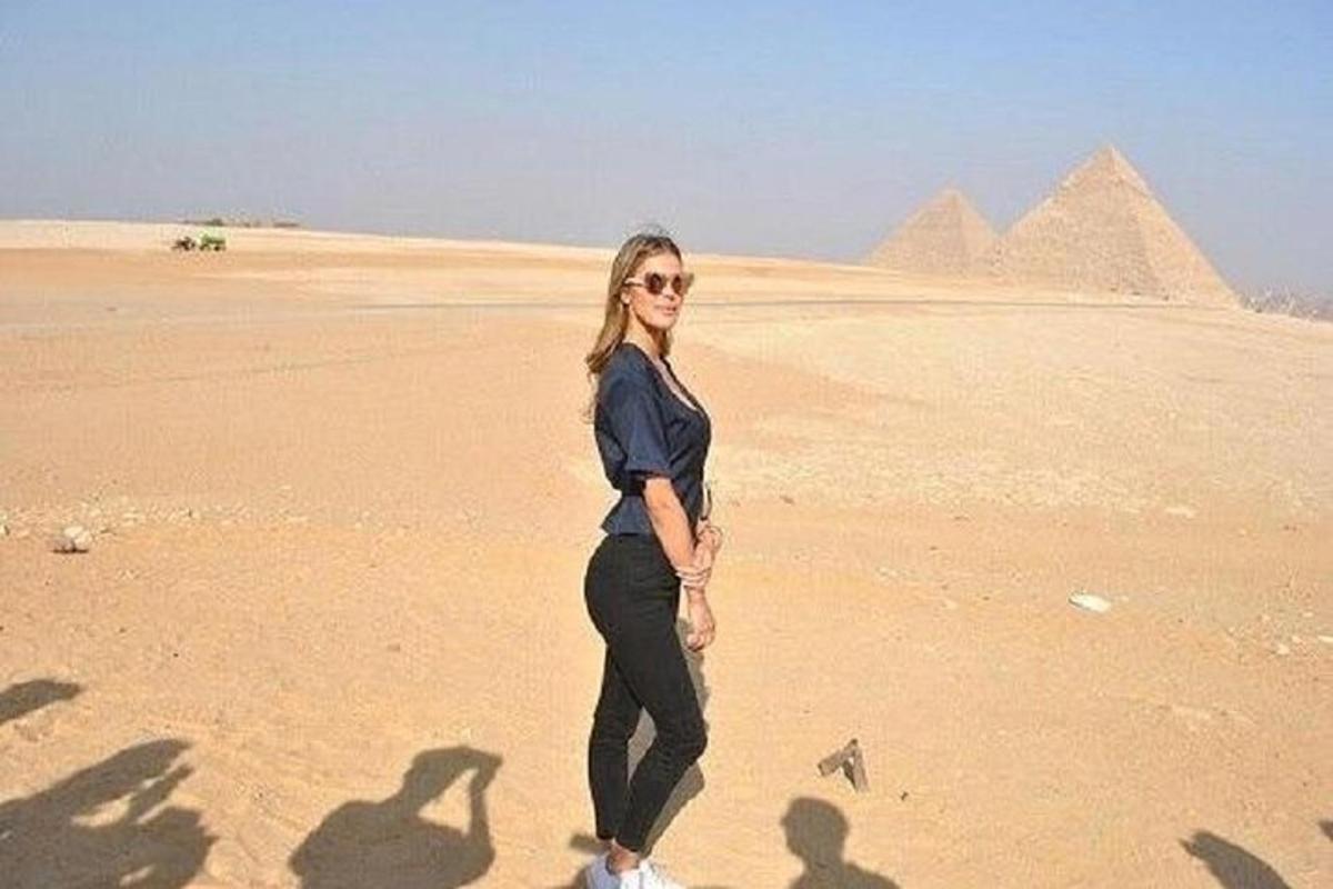 žena stojící v poušti s pyramidami v pozadí