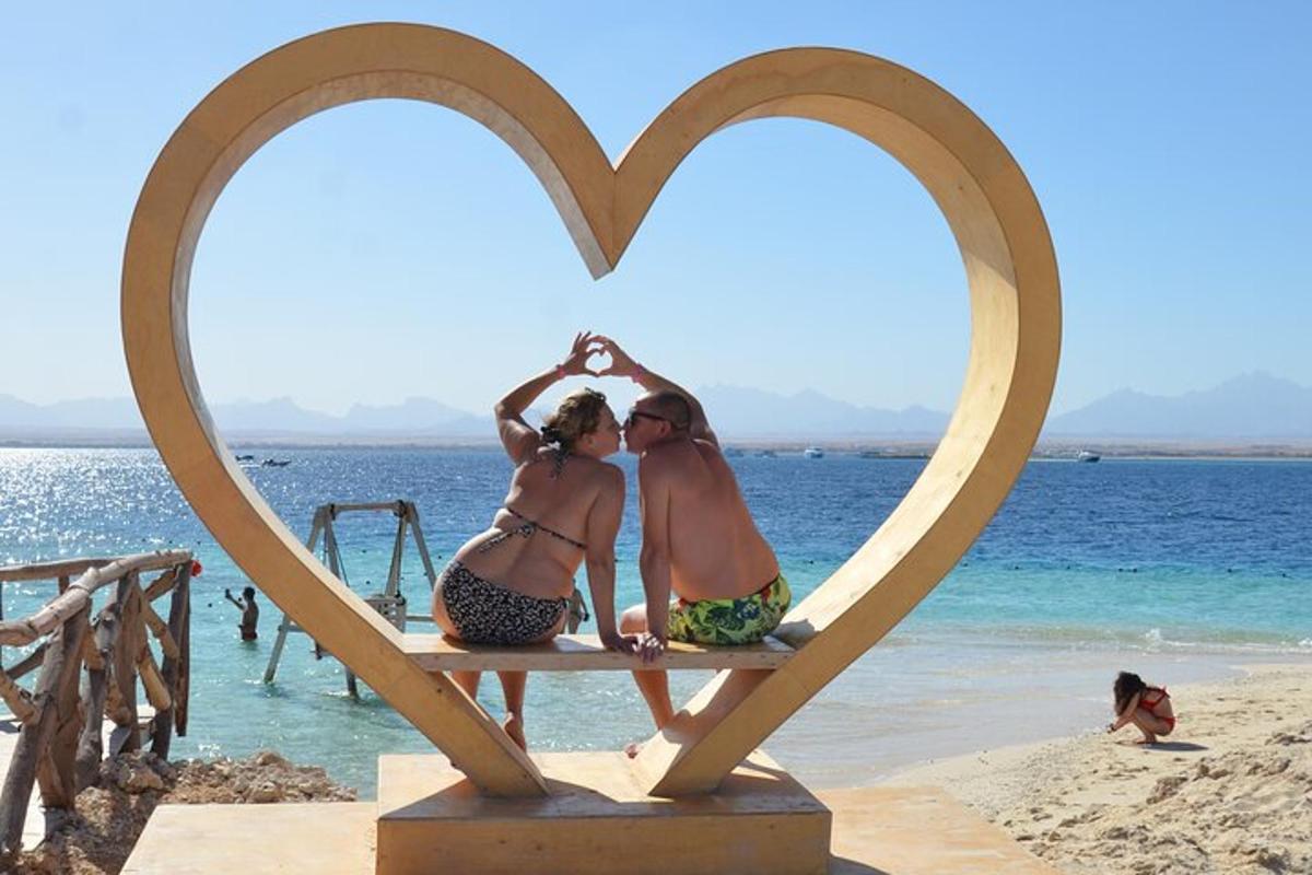 dalawang babaeng nakaupo sa isang heart sculpture sa beach
