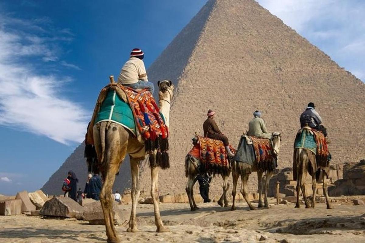Skupina lidí jedoucích na velbloudech před pyramidami