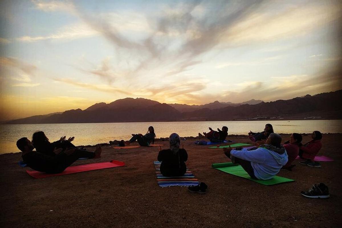 un grup de persones assegudes a la platja mirant la posta de sol