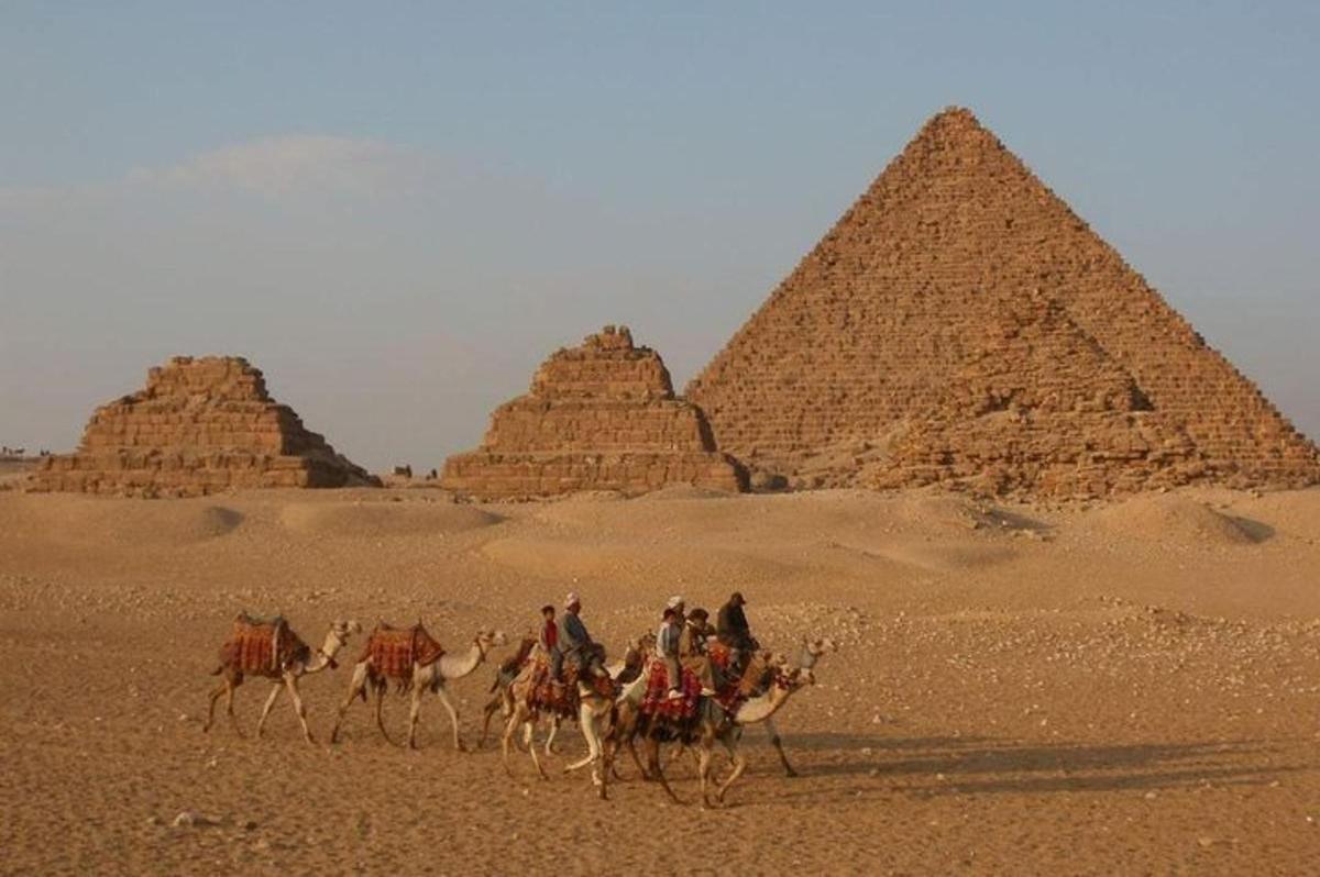 Skupina lidí jedoucích na velbloudech před pyramidami