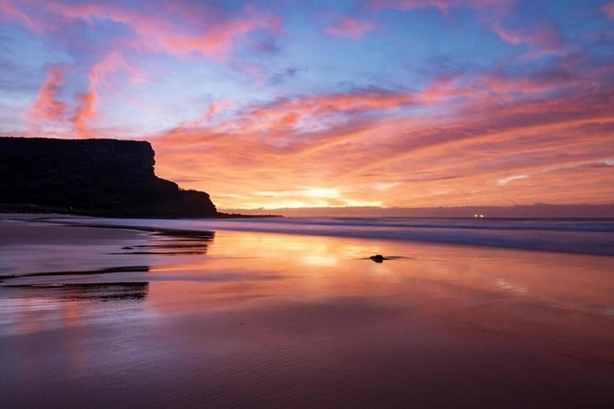 um pôr do sol na praia com uma pedra na água