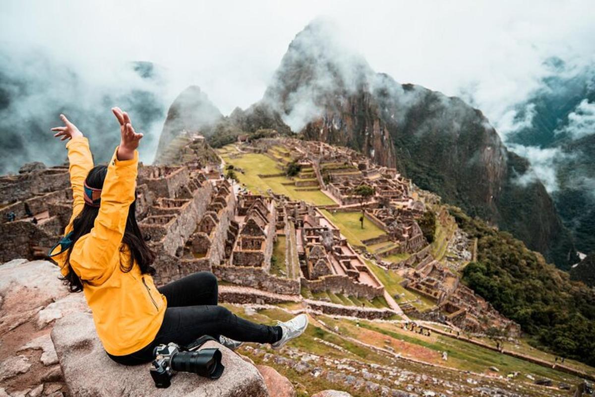 một người phụ nữ ngồi trên một tảng đá với hai tay giơ lên nhìn đống đổ nát