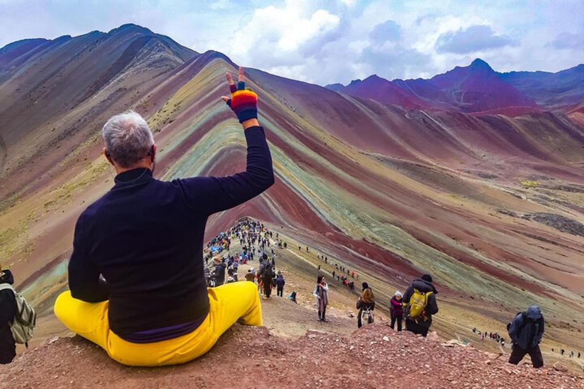 Un hombre sentado en una colina mirando hacia una montaña.