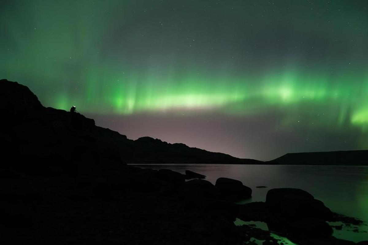 maður stendur við bakka stöðuvatns undir norðurljósum