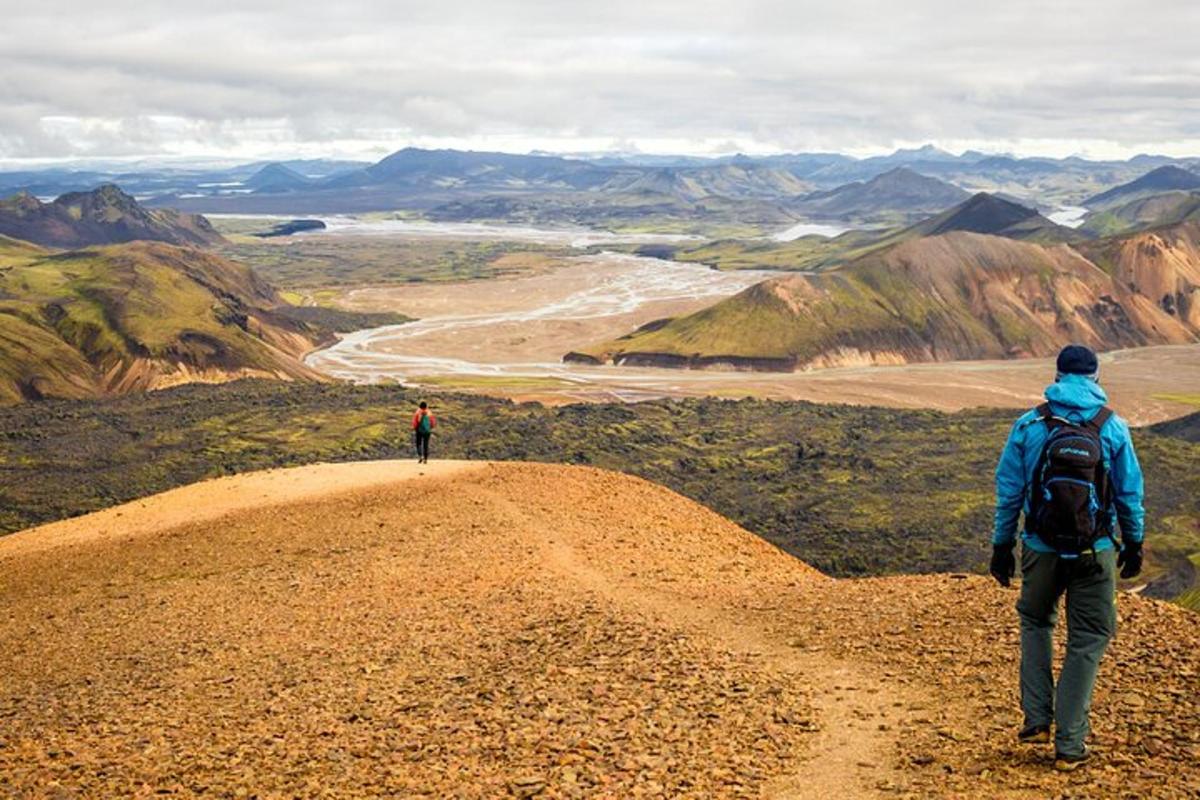 two people walking on a dirt road in the mountains