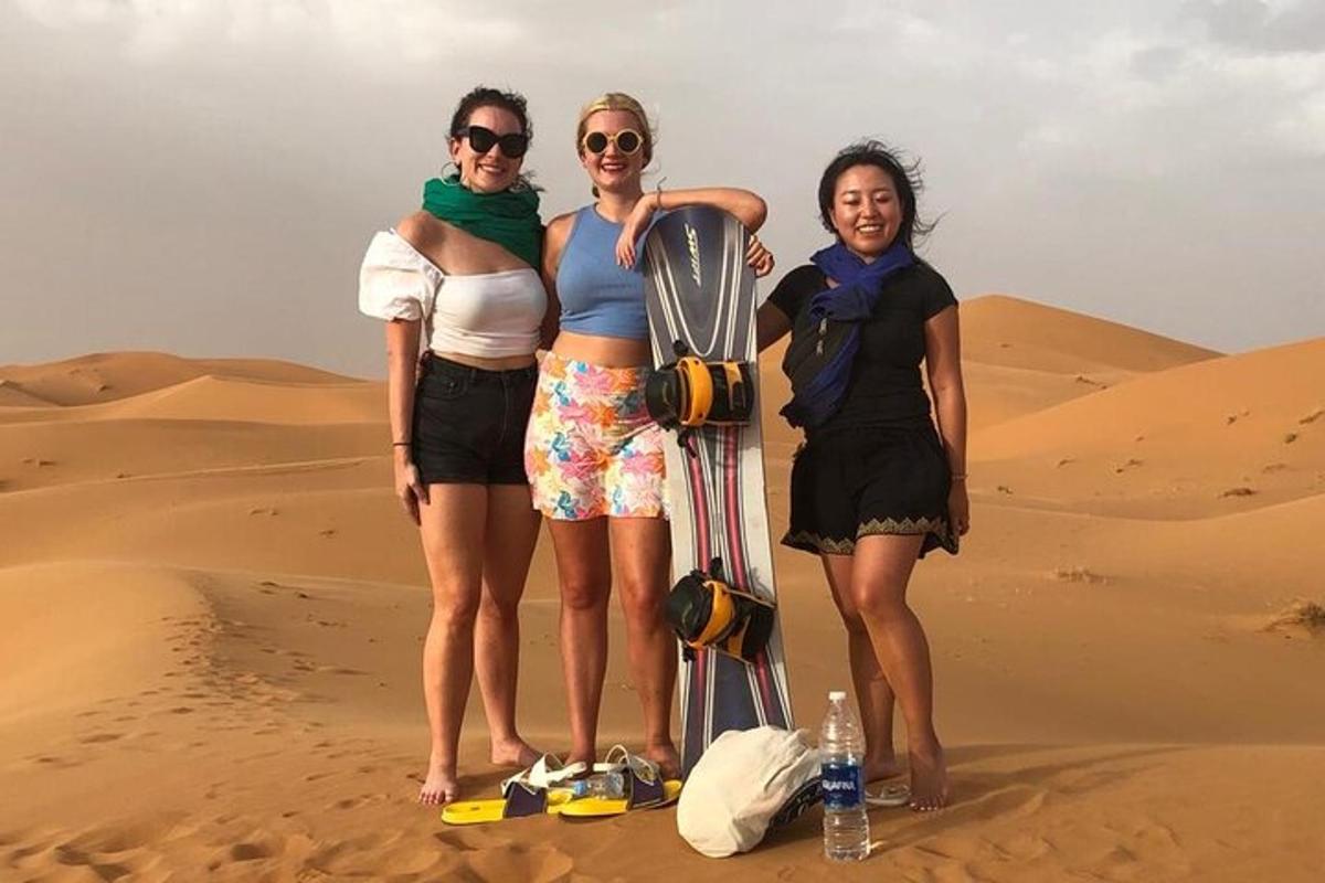 três mulheres em pé no deserto com uma prancha de snowboard