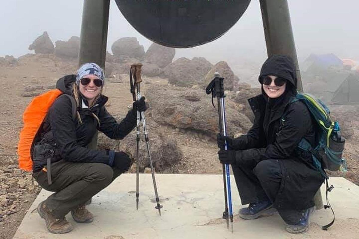 duas mulheres posando para uma foto no topo de uma montanha