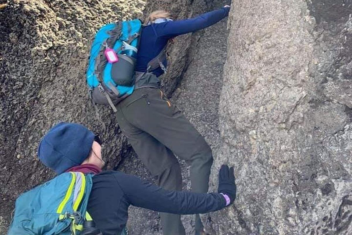 to personer som klatrer på en stein med en ryggsekk