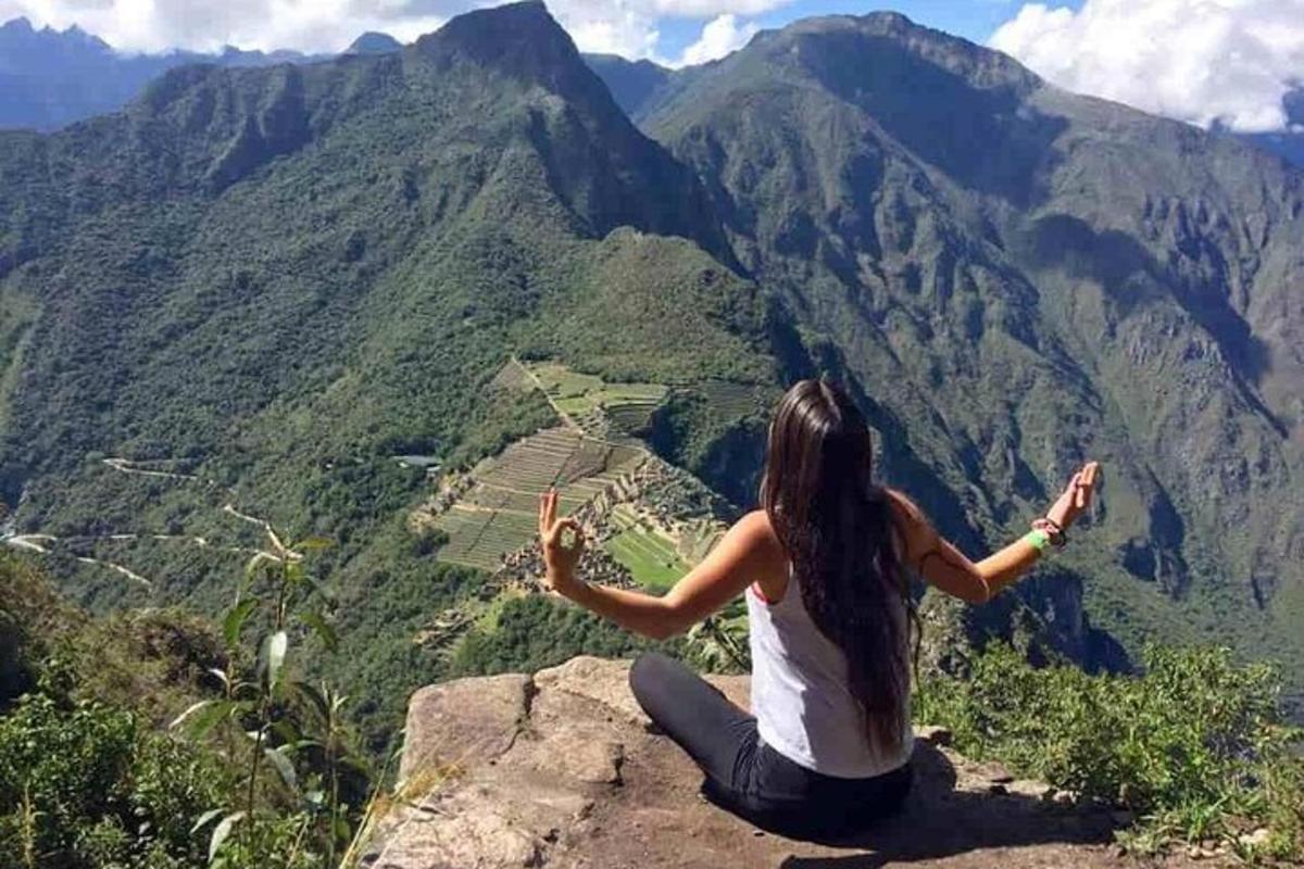 seorang wanita duduk di tepi tebing sambil melihat gunung