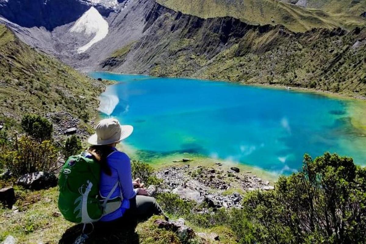 una dona asseguda en un turó mirant un llac blau