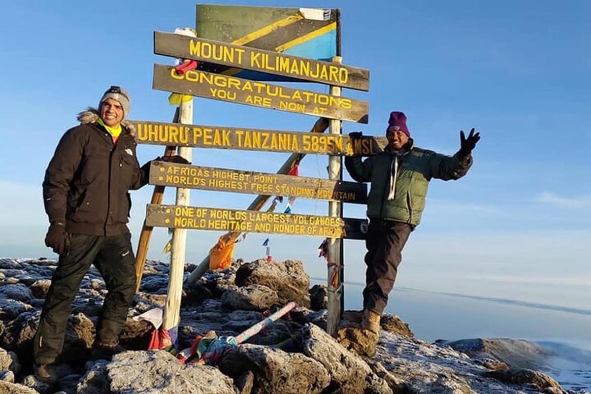 dwóch mężczyzn stojących obok znaku na szczycie góry