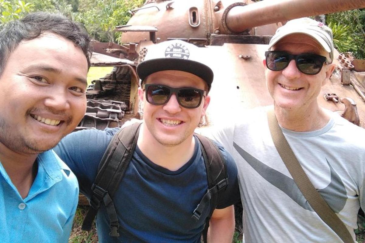 Tres hombres posando para una foto frente a un tanque