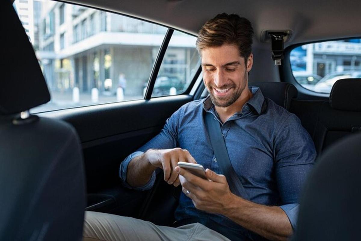 een man die op de achterbank van een auto zit en naar zijn mobiele telefoon kijkt