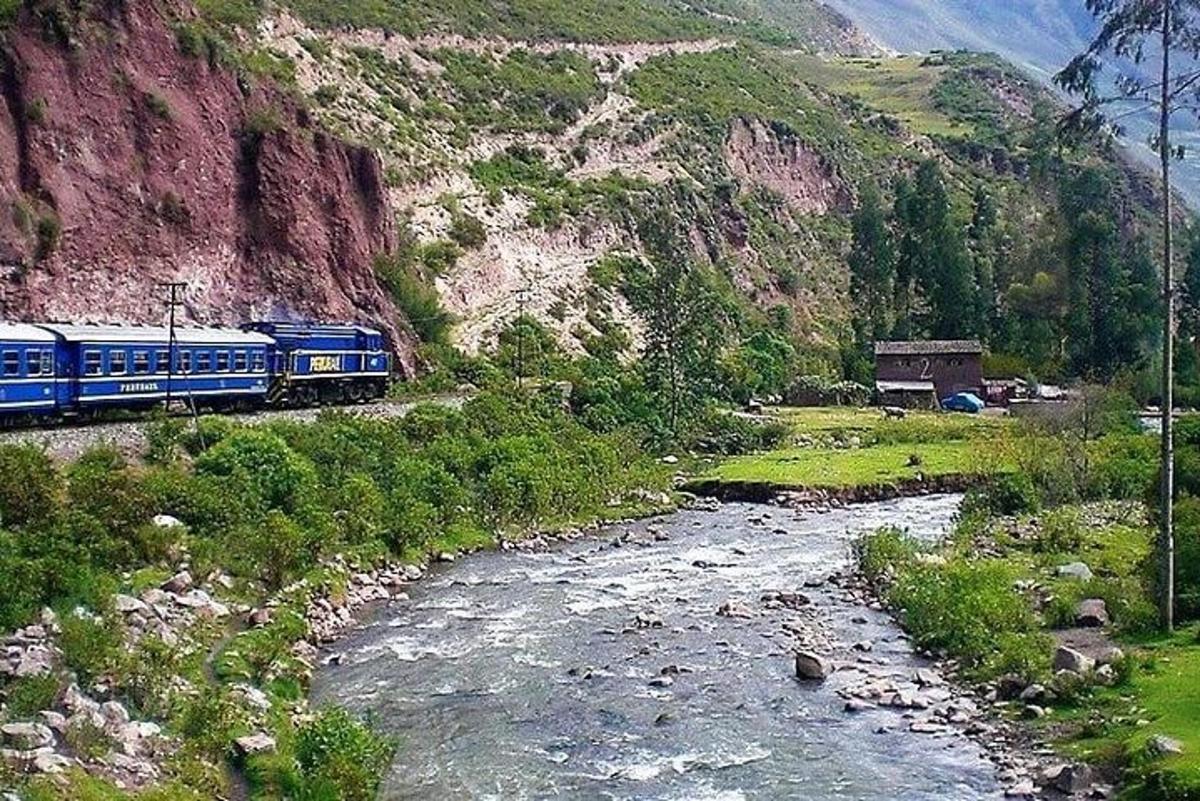 a train traveling along a river next to a mountain
