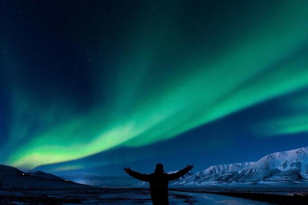 Una persona parada con los brazos extendidos frente a la aurora.