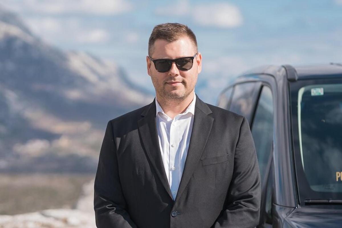 en mann i dress og solbriller som står ved siden av en bil