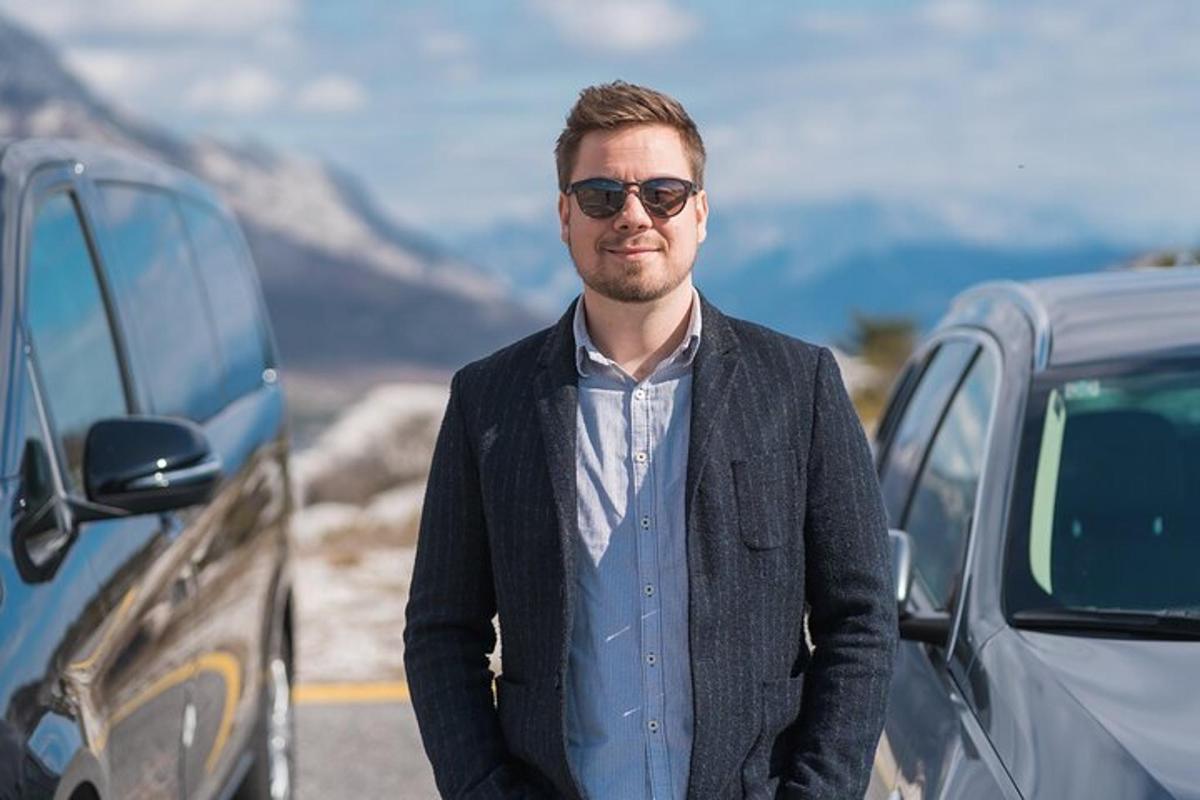 en mann med solbriller som står ved siden av en bil