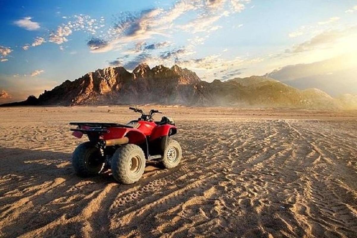 Un vehículo todo terreno rojo estacionado en el desierto con una montaña al fondo.