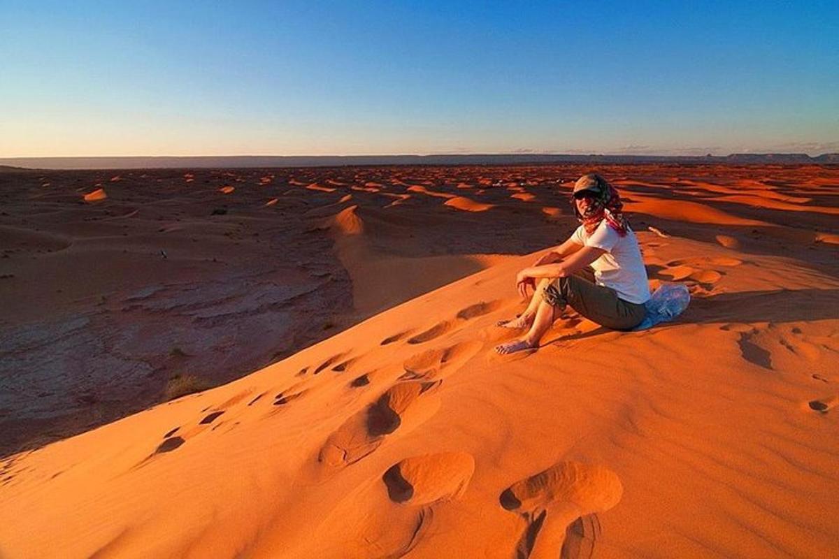 a man sitting on a sand dune in the desert