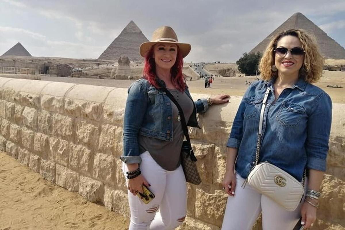 two women standing next to a stone wall in front of the pyramids