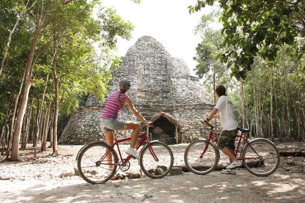 Două persoane mergând cu bicicleta în fața unei piramide