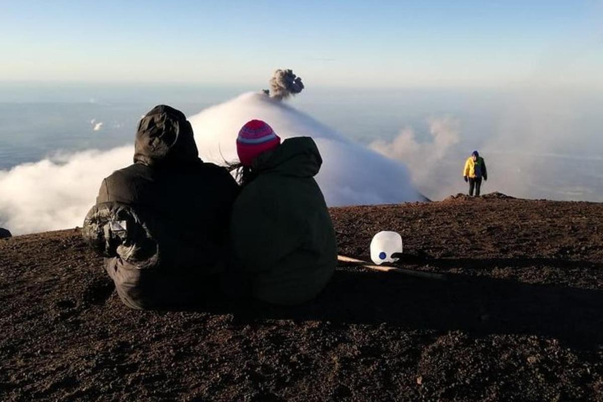 two people sitting on a hill looking at a volcano