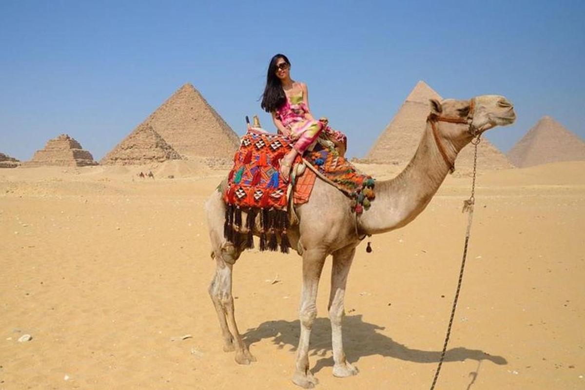žena sedící na velbloudovi před pyramidami