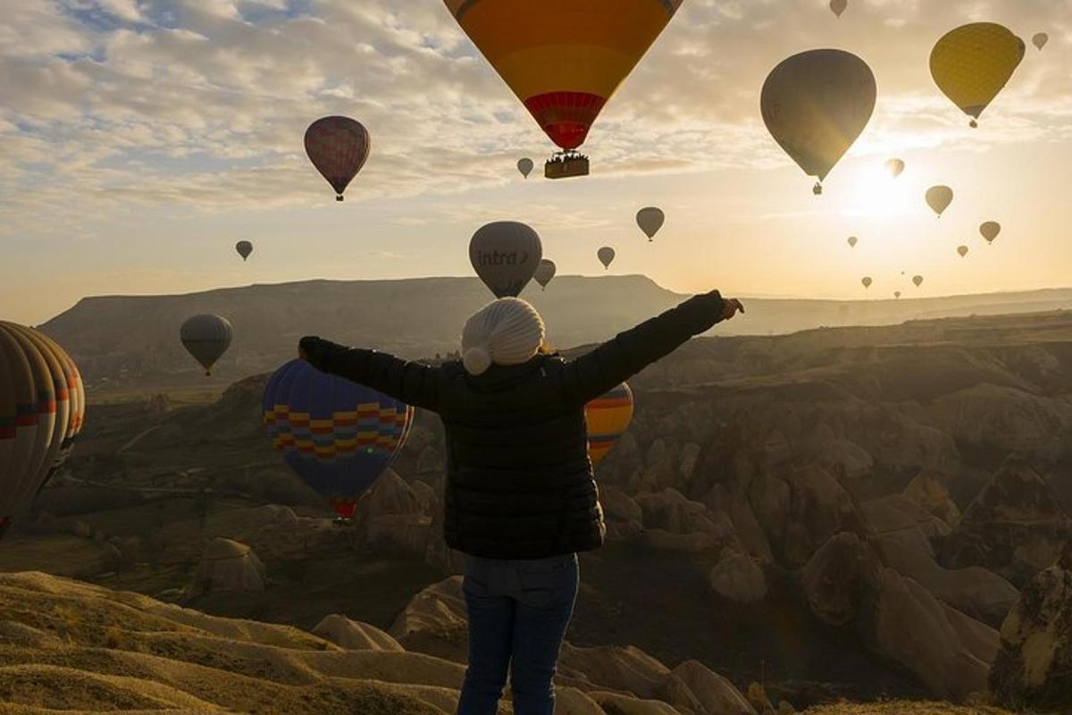 a person standing on a mountain looking at hot air balloons