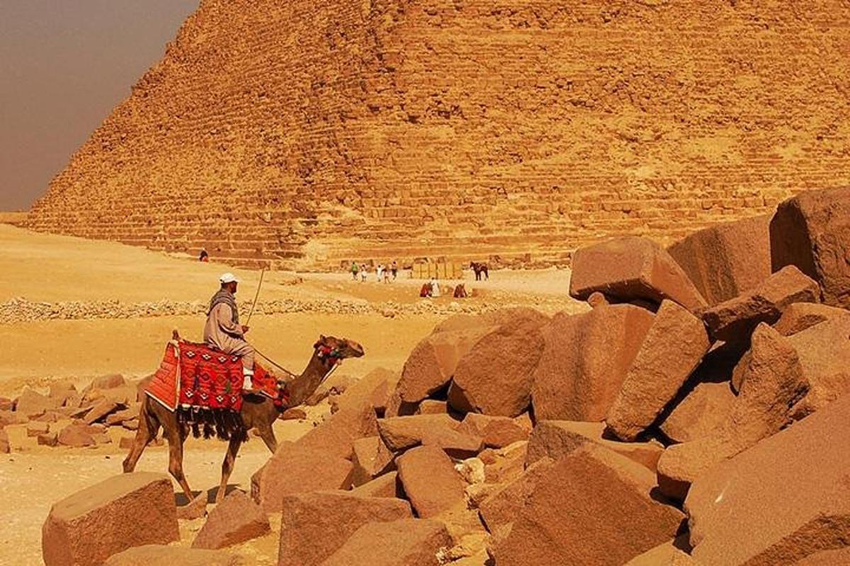 muž jedoucí na velbloudovi před pyramidou