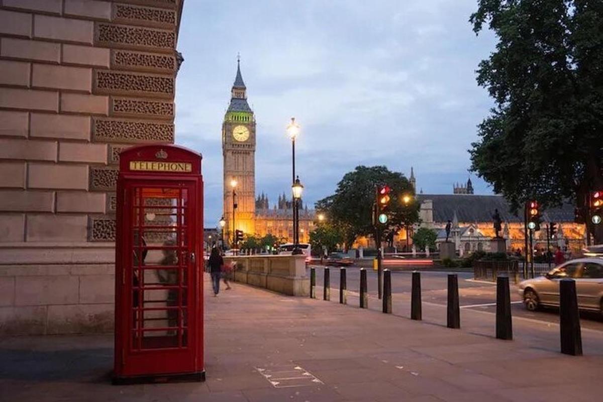 una cabina telefonica rossa su un marciapiede con una torre dell'orologio